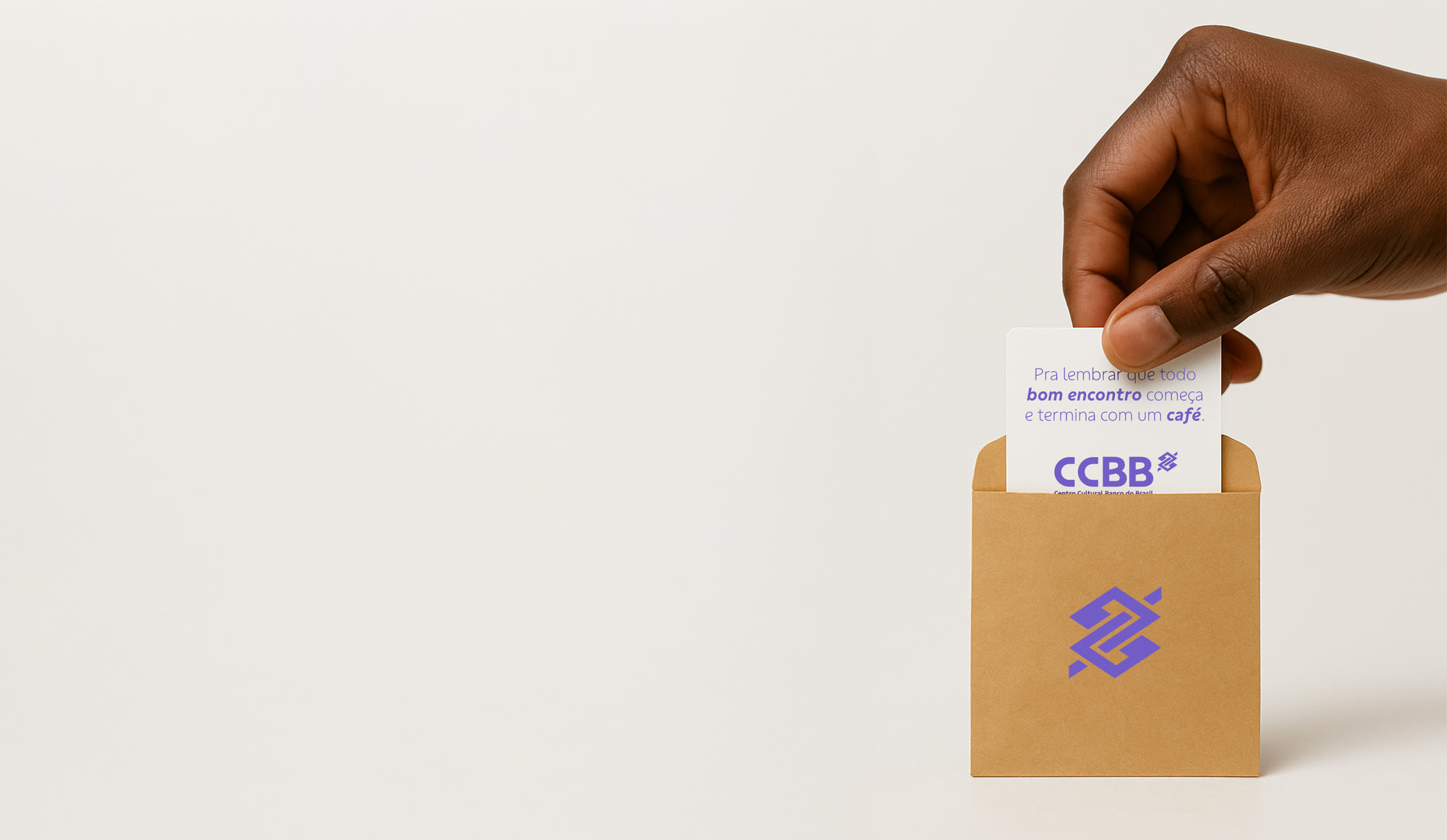 A hand placing a CCBB card in a kraft envelope with the Banco do Brasil symbol
