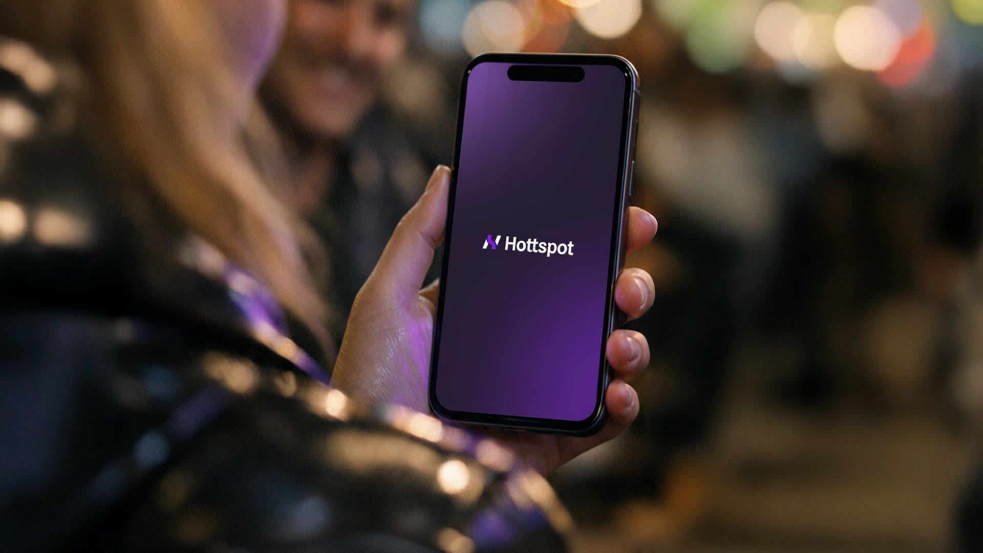 A hand holding a phone with the HottSpot splash screen on a night out